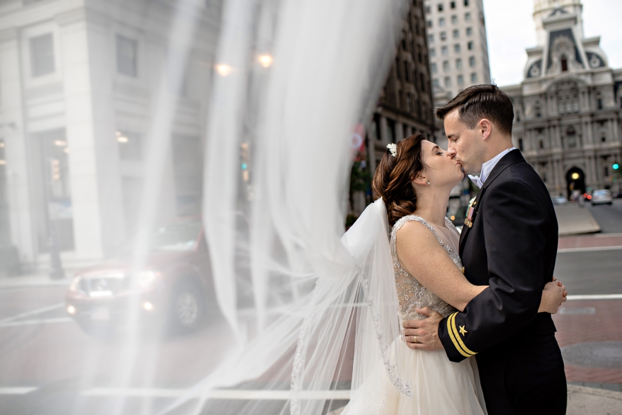A bride and groom kiss while her veil blows in the wind.